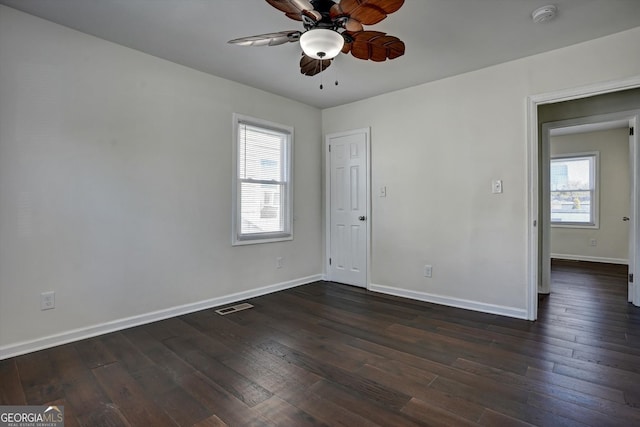 empty room featuring ceiling fan, dark wood-type flooring, and a healthy amount of sunlight