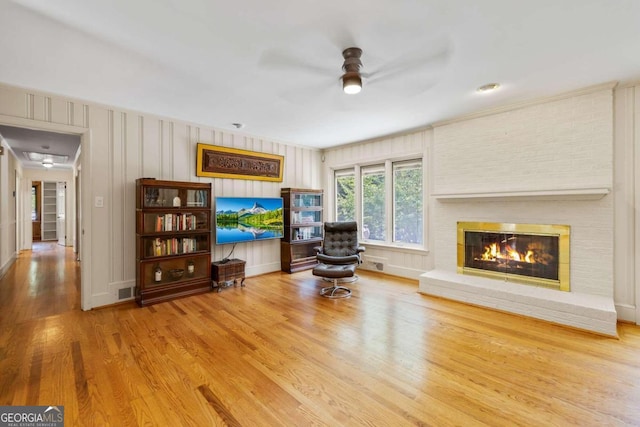 living area with a brick fireplace, ceiling fan, and hardwood / wood-style flooring