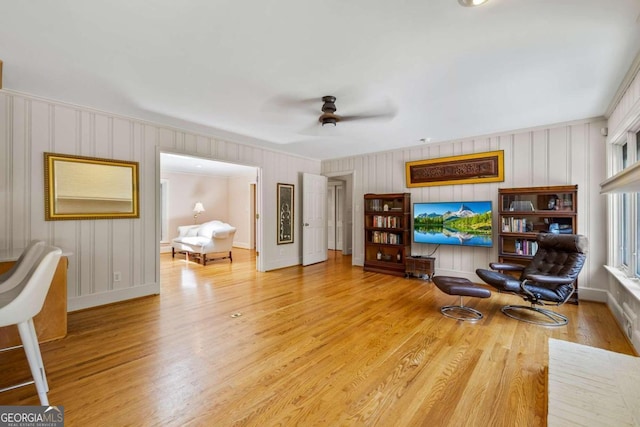 sitting room with ceiling fan, ornamental molding, wooden walls, and light hardwood / wood-style flooring