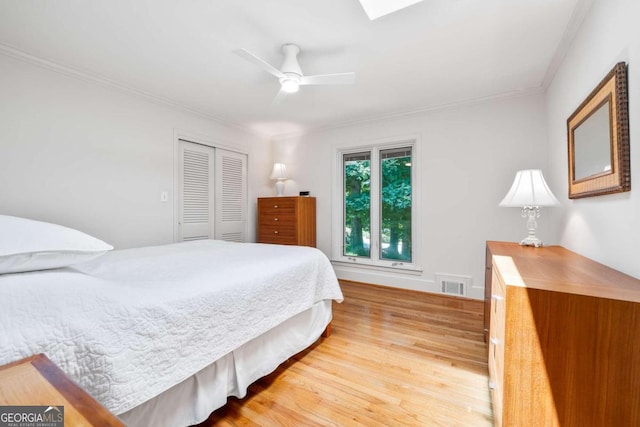 bedroom featuring a skylight, ornamental molding, ceiling fan, wood-type flooring, and a closet