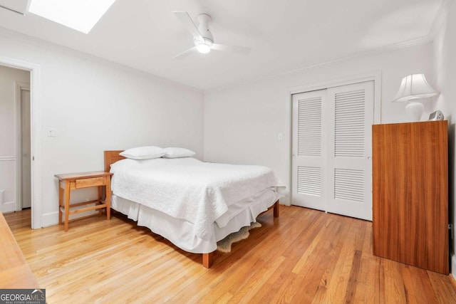 bedroom featuring a skylight, ceiling fan, light hardwood / wood-style floors, a closet, and ornamental molding