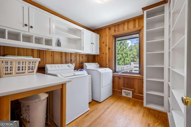 laundry room featuring washer and dryer, light hardwood / wood-style flooring, cabinets, and wooden walls