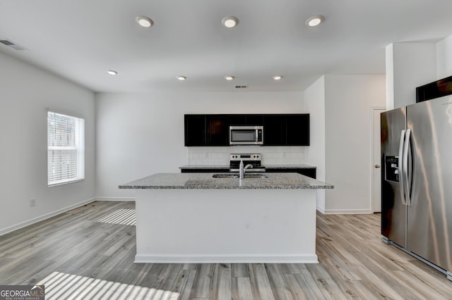 kitchen with light stone countertops, stainless steel appliances, a kitchen island with sink, and sink