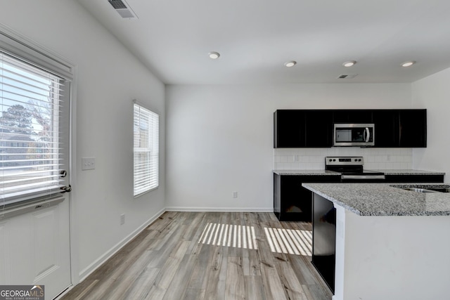 kitchen with sink, stainless steel appliances, light stone counters, light hardwood / wood-style flooring, and decorative backsplash