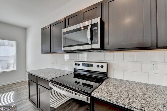 kitchen with decorative backsplash, appliances with stainless steel finishes, light stone counters, dark brown cabinets, and light hardwood / wood-style flooring