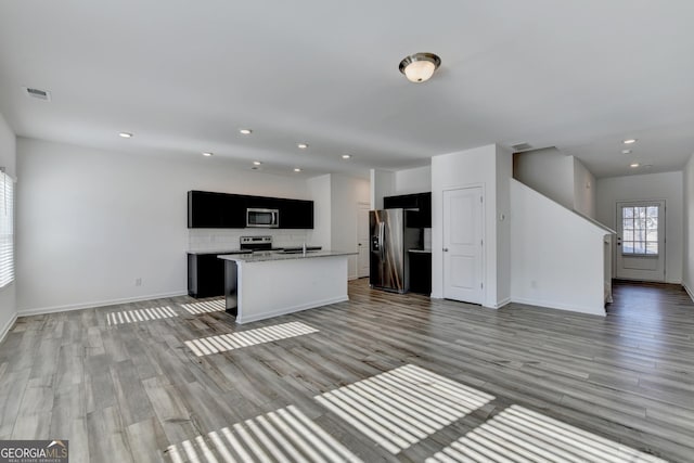 kitchen with backsplash, light hardwood / wood-style floors, a kitchen island with sink, and appliances with stainless steel finishes