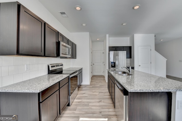 kitchen with a center island with sink, sink, light wood-type flooring, dark brown cabinets, and stainless steel appliances