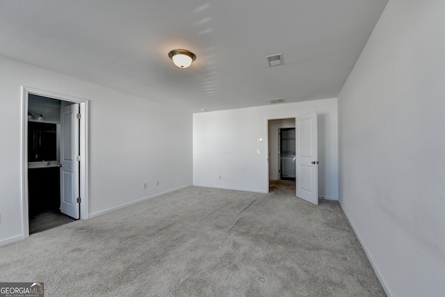 unfurnished bedroom with ensuite bathroom and light carpet