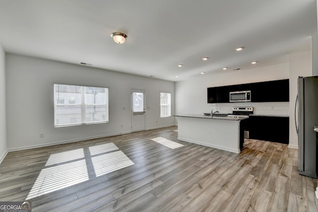 kitchen featuring sink, stainless steel appliances, light hardwood / wood-style flooring, decorative backsplash, and a center island with sink