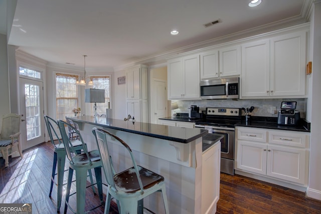 kitchen with white cabinetry, a breakfast bar area, appliances with stainless steel finishes, and dark wood-type flooring