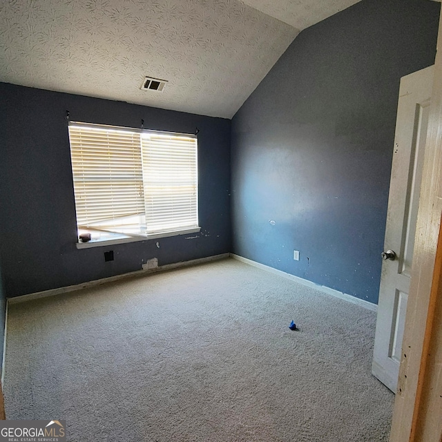 carpeted empty room featuring lofted ceiling and a textured ceiling