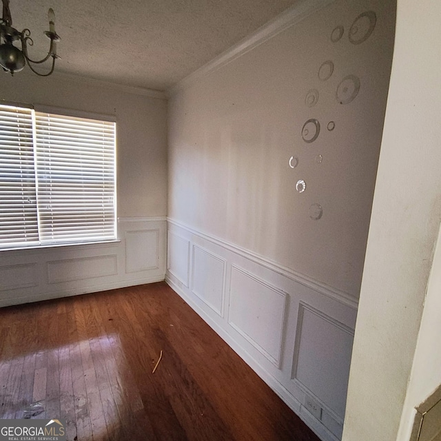 spare room with a chandelier, a textured ceiling, crown molding, and dark wood-type flooring