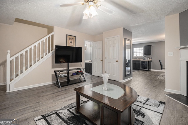 living room featuring ceiling fan, sink, beverage cooler, hardwood / wood-style floors, and a textured ceiling