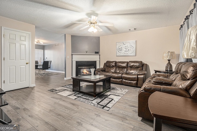 living room with ceiling fan, light hardwood / wood-style floors, and a textured ceiling