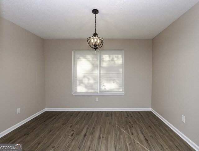 empty room featuring dark wood-type flooring, a textured ceiling, and an inviting chandelier