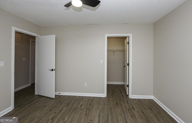 unfurnished bedroom with dark hardwood / wood-style flooring, a textured ceiling, ceiling fan, a spacious closet, and a closet