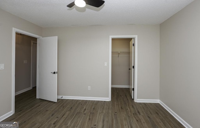 unfurnished bedroom featuring a textured ceiling, dark wood-type flooring, baseboards, a spacious closet, and a closet