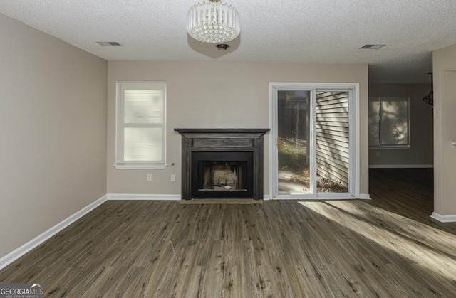 unfurnished living room with a fireplace with flush hearth, dark wood finished floors, visible vents, and baseboards