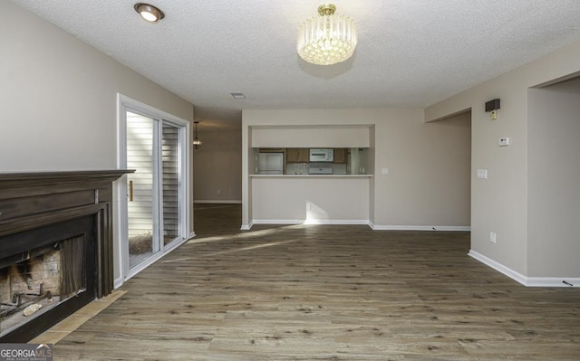 unfurnished living room with a fireplace, a textured ceiling, baseboards, and wood finished floors