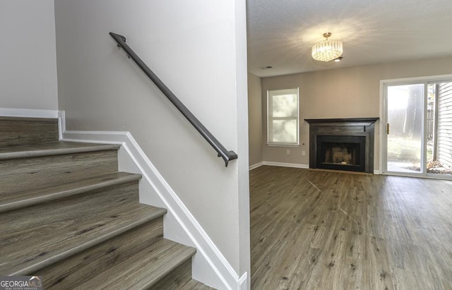 staircase featuring visible vents, baseboards, wood finished floors, a fireplace, and a chandelier