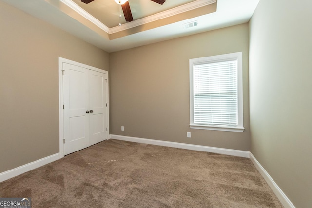 empty room with a raised ceiling, ornamental molding, carpet flooring, and ceiling fan