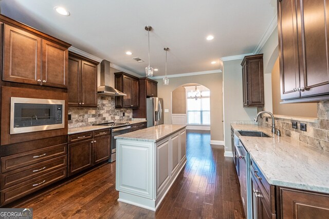 kitchen with stainless steel appliances, wall chimney range hood, dark hardwood / wood-style floors, decorative light fixtures, and a kitchen island