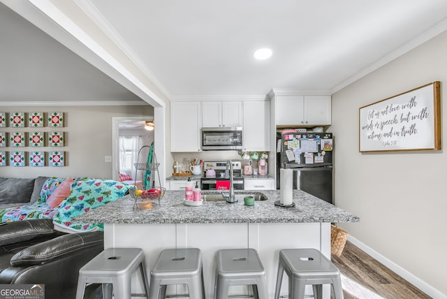 kitchen featuring a kitchen breakfast bar, hardwood / wood-style flooring, light stone countertops, appliances with stainless steel finishes, and white cabinetry