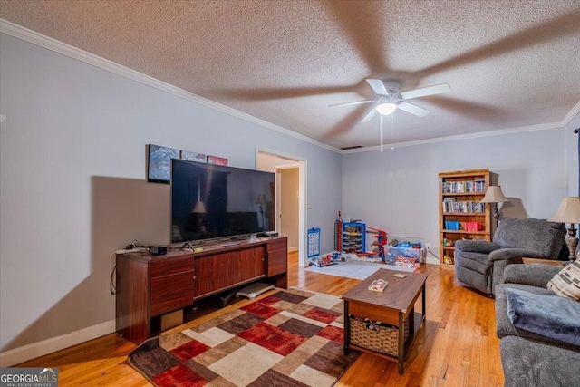 living room featuring ceiling fan, ornamental molding, a textured ceiling, and light wood-type flooring