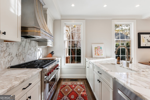 kitchen featuring light stone countertops, sink, stainless steel appliances, and wall chimney range hood