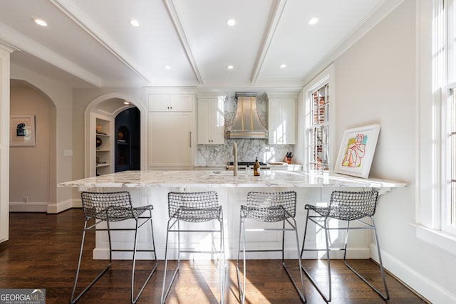 kitchen featuring light stone countertops, a breakfast bar, dark wood-type flooring, and wall chimney range hood