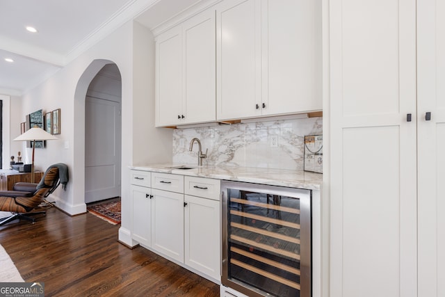 bar with light stone countertops, dark hardwood / wood-style flooring, ornamental molding, beverage cooler, and white cabinetry