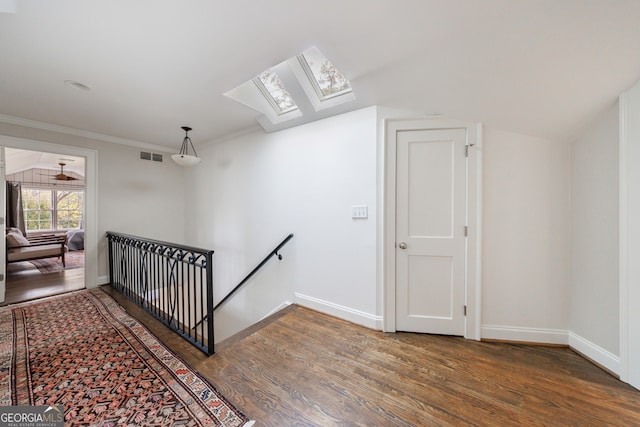 stairway with ceiling fan, vaulted ceiling with skylight, wood-type flooring, and ornamental molding