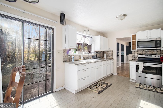 kitchen with decorative backsplash, white cabinets, light wood-type flooring, and appliances with stainless steel finishes