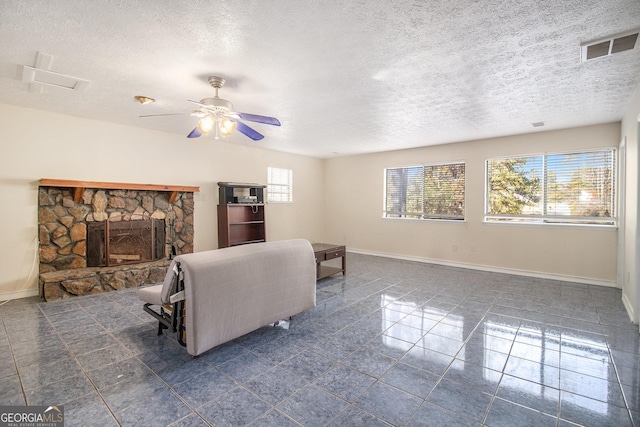 tiled living room featuring a textured ceiling, a stone fireplace, and ceiling fan