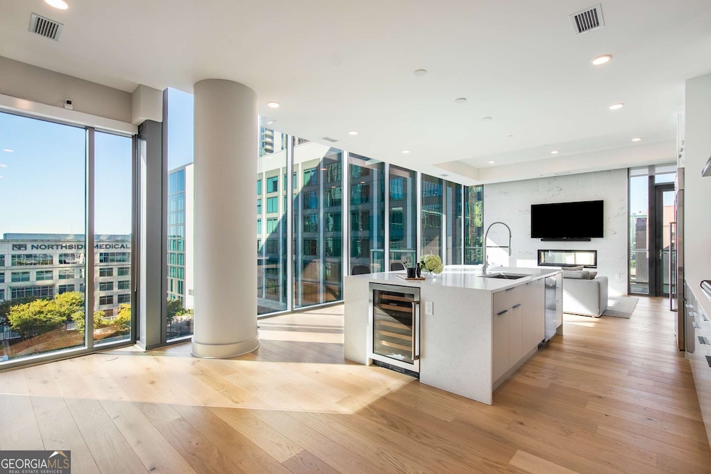 kitchen with a center island with sink, a healthy amount of sunlight, light wood-type flooring, and beverage cooler