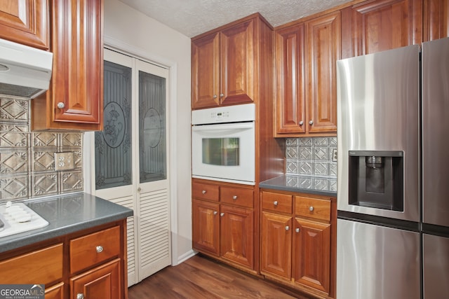 kitchen with dark wood-type flooring, tasteful backsplash, stainless steel refrigerator with ice dispenser, oven, and a textured ceiling