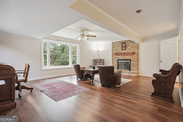 living room featuring ceiling fan, dark hardwood / wood-style flooring, ornamental molding, and a brick fireplace