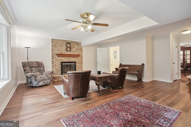 living room with a fireplace, ceiling fan, crown molding, and wood-type flooring