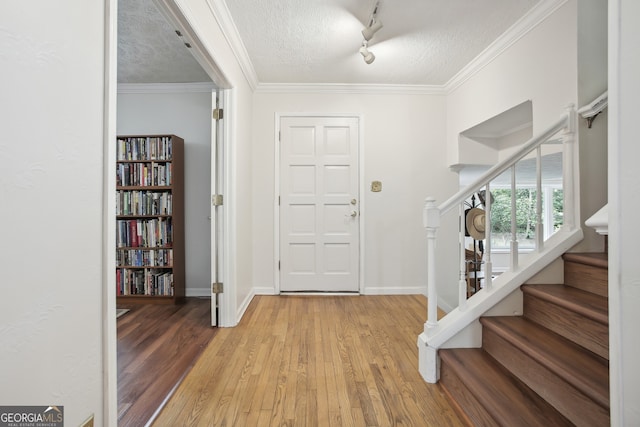 entryway with light hardwood / wood-style flooring, rail lighting, a textured ceiling, and ornamental molding