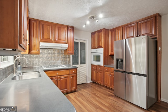 kitchen featuring appliances with stainless steel finishes, backsplash, a textured ceiling, sink, and light hardwood / wood-style floors