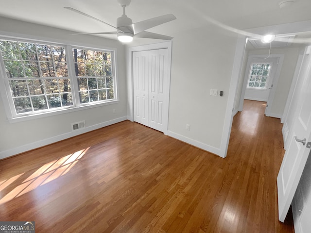 unfurnished bedroom featuring wood-type flooring, a closet, multiple windows, and ceiling fan