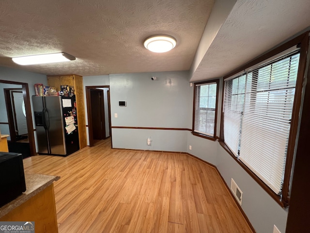 kitchen with light wood finished floors, visible vents, baseboards, stainless steel fridge with ice dispenser, and light countertops