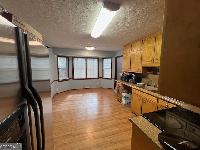 kitchen featuring brown cabinets, light countertops, visible vents, light wood-style floors, and freestanding refrigerator