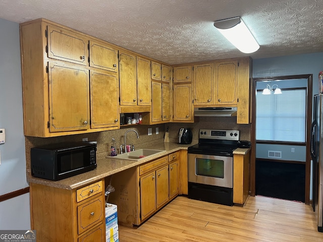 kitchen featuring under cabinet range hood, a sink, light countertops, black appliances, and brown cabinetry