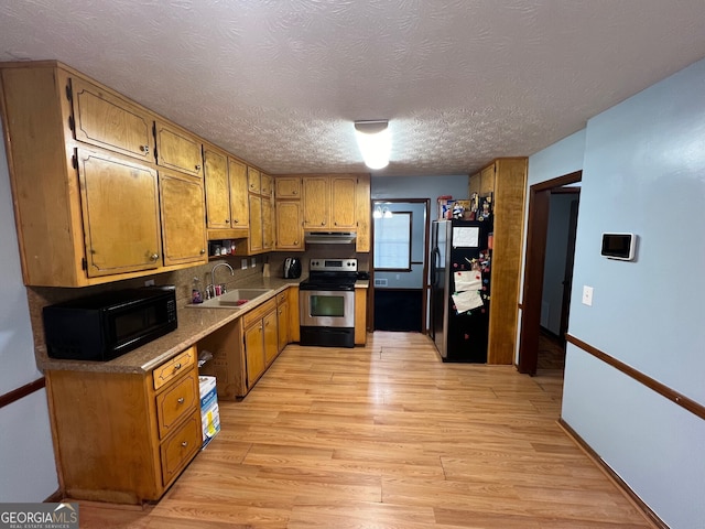 kitchen with light wood finished floors, light countertops, brown cabinetry, a sink, and black appliances