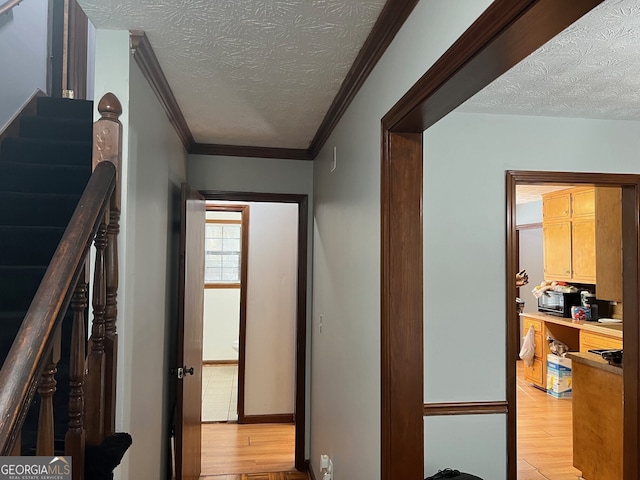 corridor with stairs, light wood finished floors, a textured ceiling, and crown molding