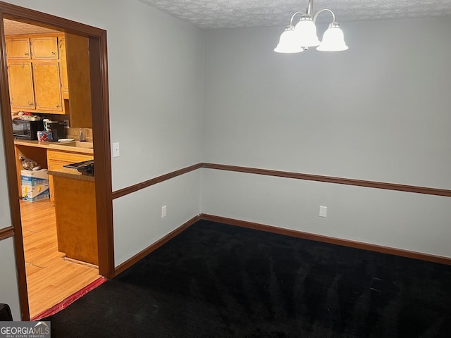 unfurnished dining area featuring light wood finished floors, a sink, a textured ceiling, a chandelier, and baseboards