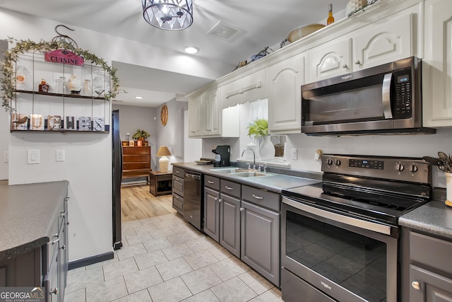 kitchen featuring dark countertops, stainless steel appliances, gray cabinetry, white cabinetry, and a sink