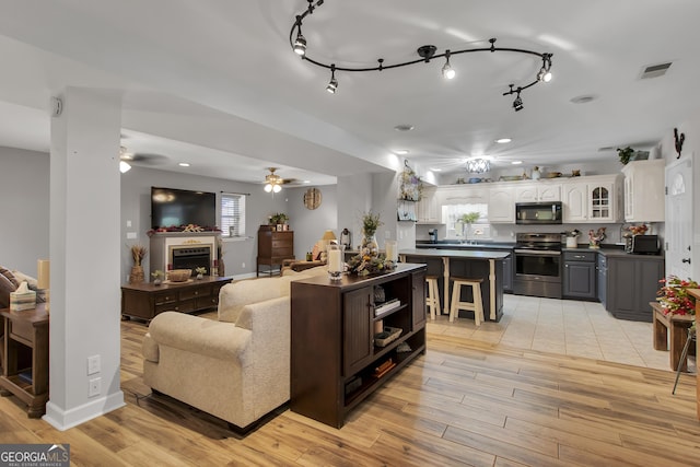 living room with a fireplace, visible vents, ceiling fan, light wood-type flooring, and baseboards