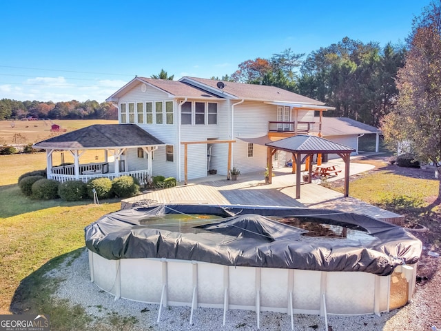 back of property featuring a yard, a covered pool, a wooden deck, and a gazebo